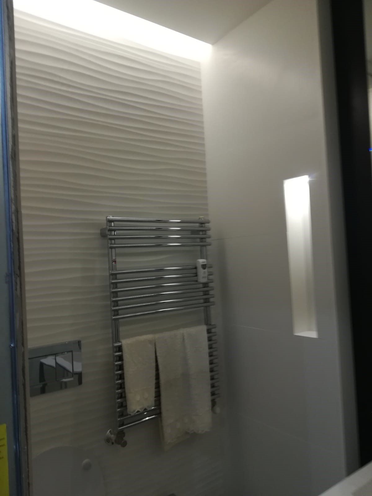 Modern bathroom with chrome towel rack, beige towel, and frosted glass shower door
