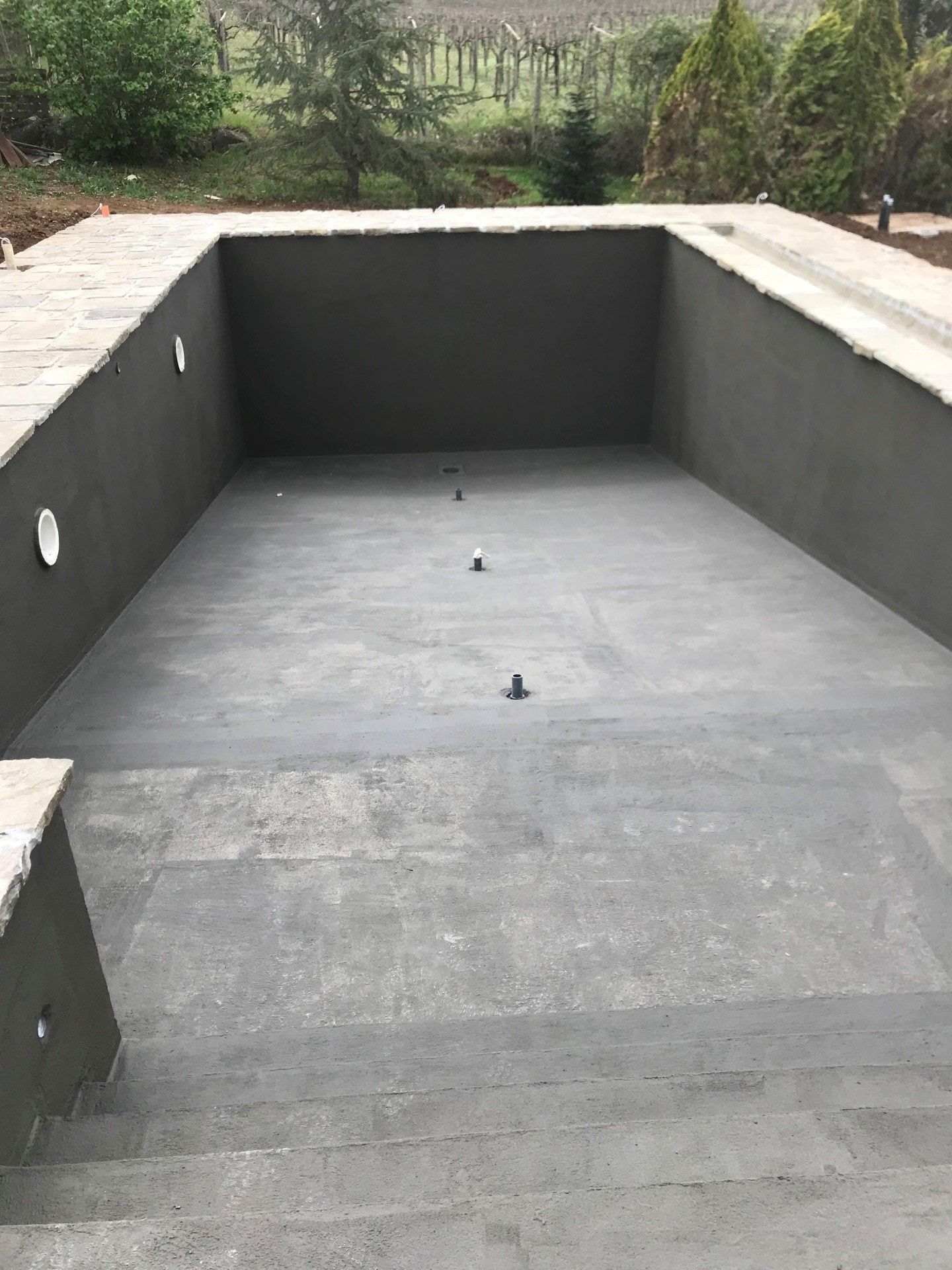 Empty rectangular concrete pool under construction, with dark coated walls and floor draining fixtures.