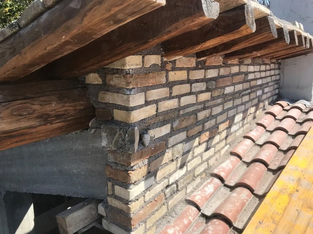 Brick chimney under a tiled roof with exposed wooden beams and nearby red roof tiles
