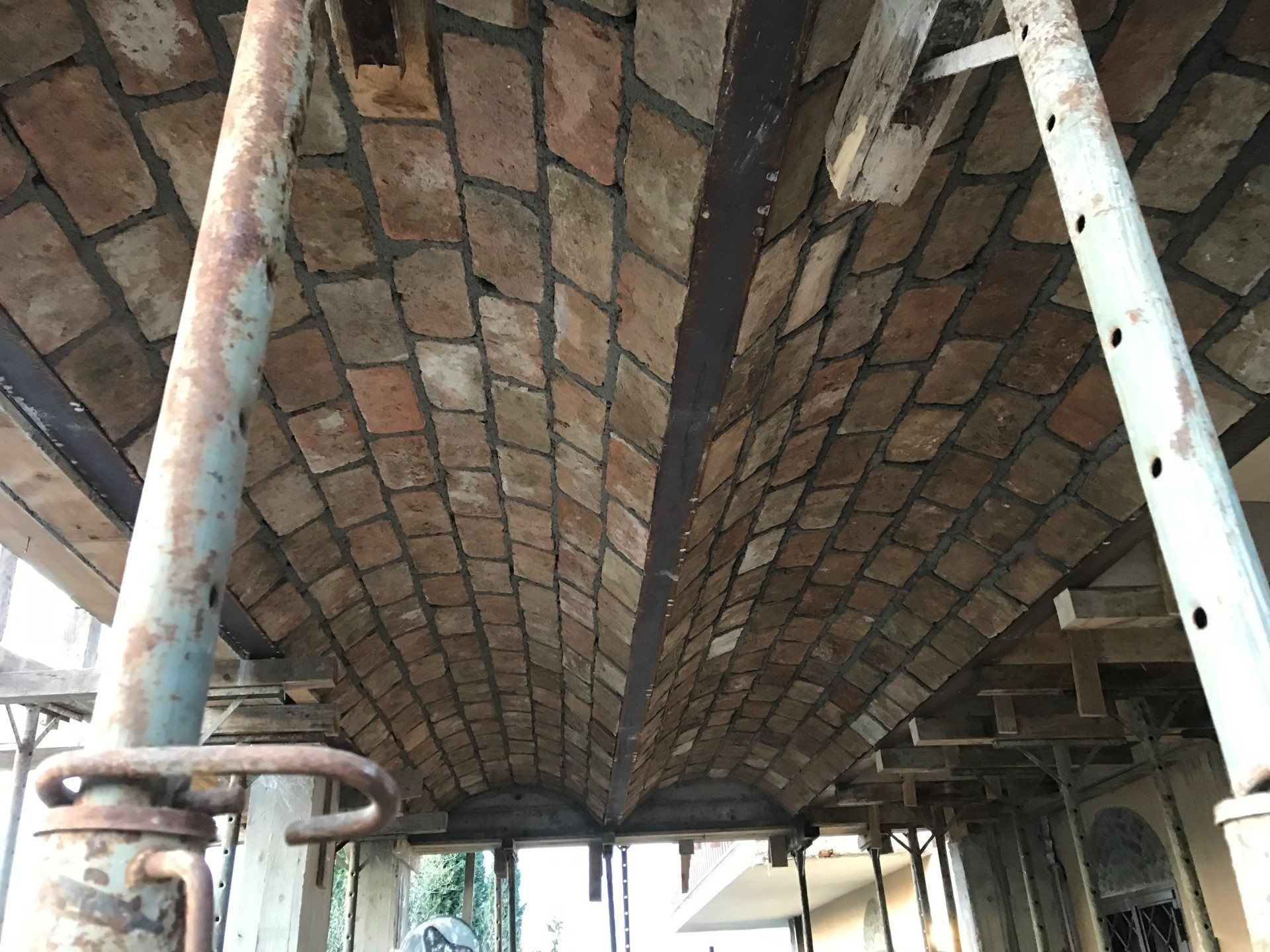 Underside of a brick arch ceiling under construction, with metal support poles in the foreground.