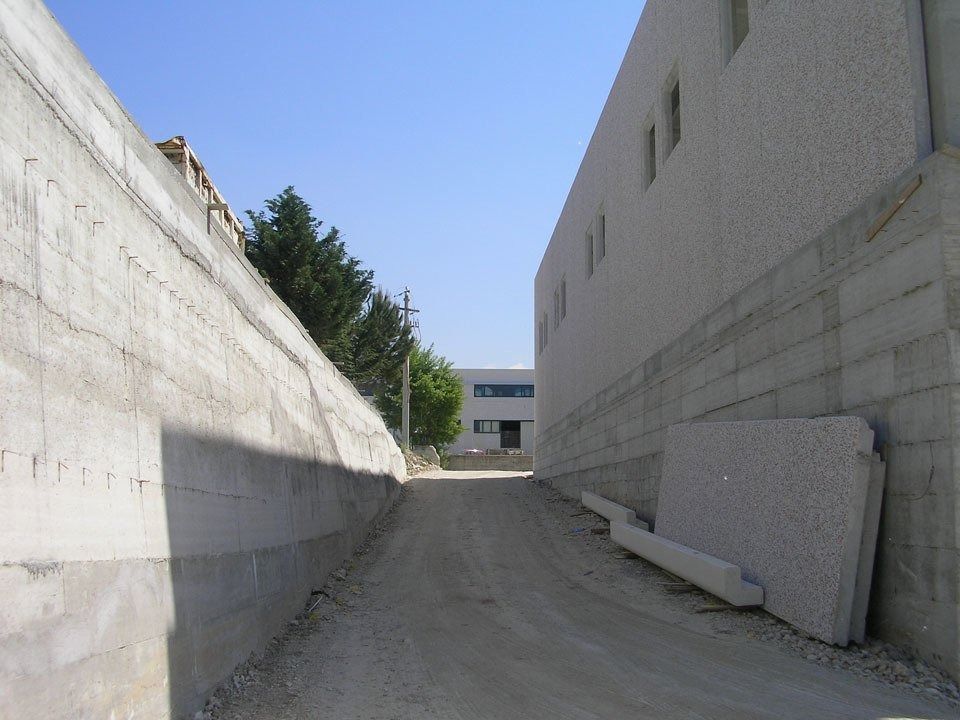 Narrow concrete alley between tall buildings, sloping uphill toward a small structure ahead