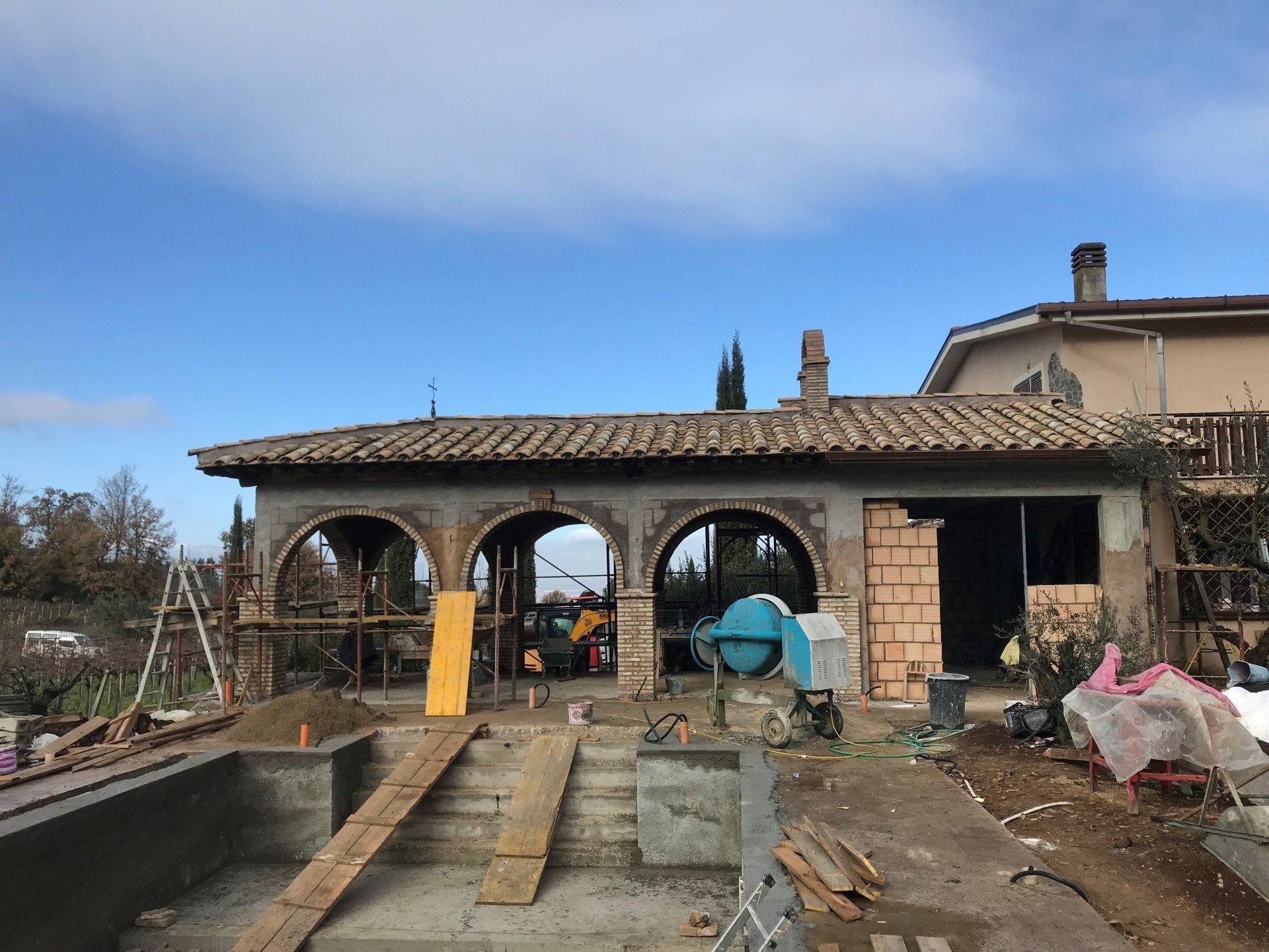 Partially built stone patio with arched openings, ramps, and construction materials outside a house
