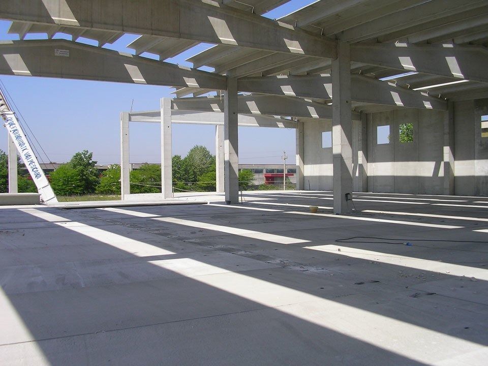 Empty concrete building interior with sunlight streaming through open walls and roof beams