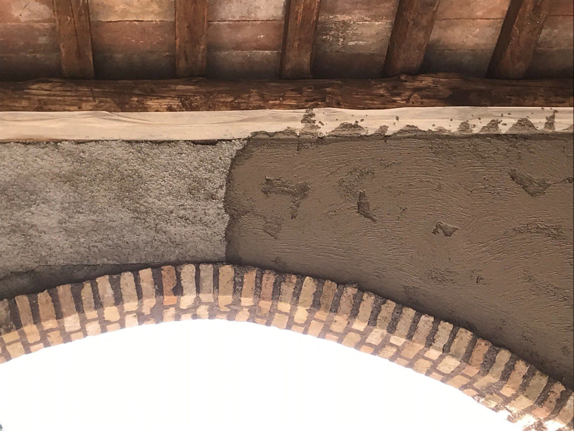 Brick arch under a wooden roof with weathered plaster walls and bright sky below