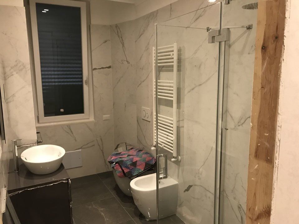Modern bathroom with marble walls, glass shower, wall-mounted towel warmer, sink, and toilet