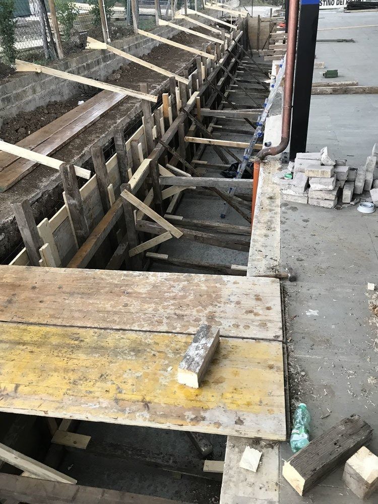 Construction site with a narrow trench, wooden planks, and scattered tools beside a concrete path
