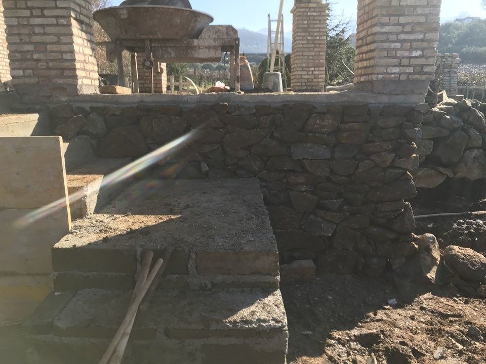 Stone patio and low wall with bright sunlight, stone pillars, and a hose spraying water across the steps