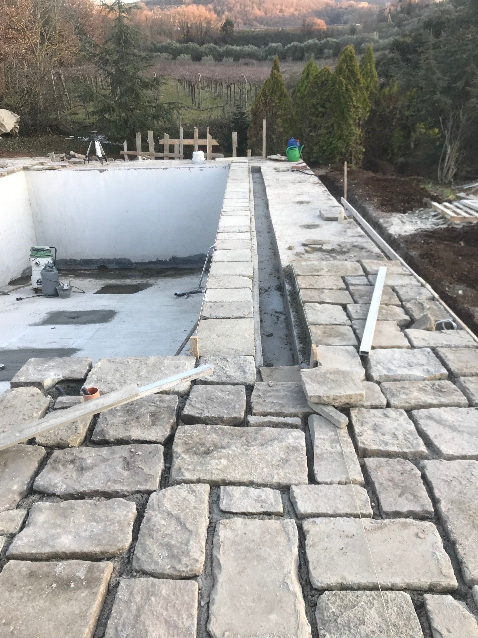 Partially built pool area with stone patio, white walls, and a narrow raised walkway.