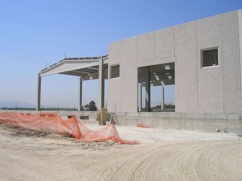 Partially built concrete house with orange construction fencing and dirt road under clear sky