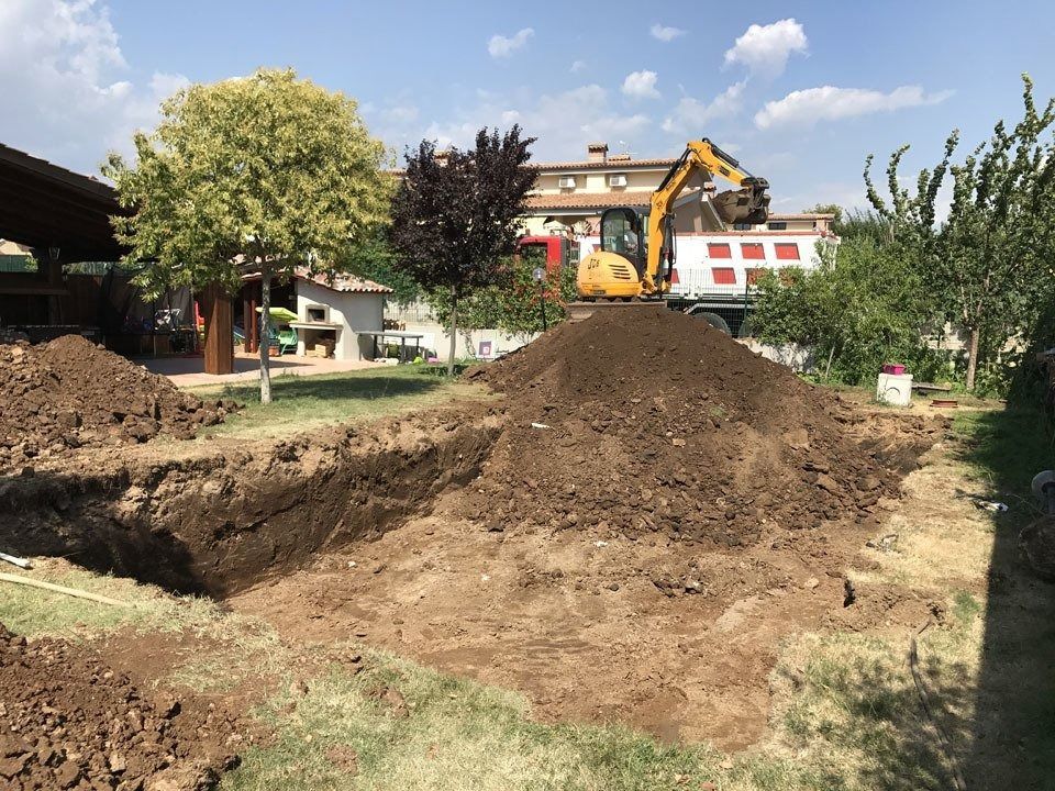 Excavator at a residential construction site beside large dirt piles and a house