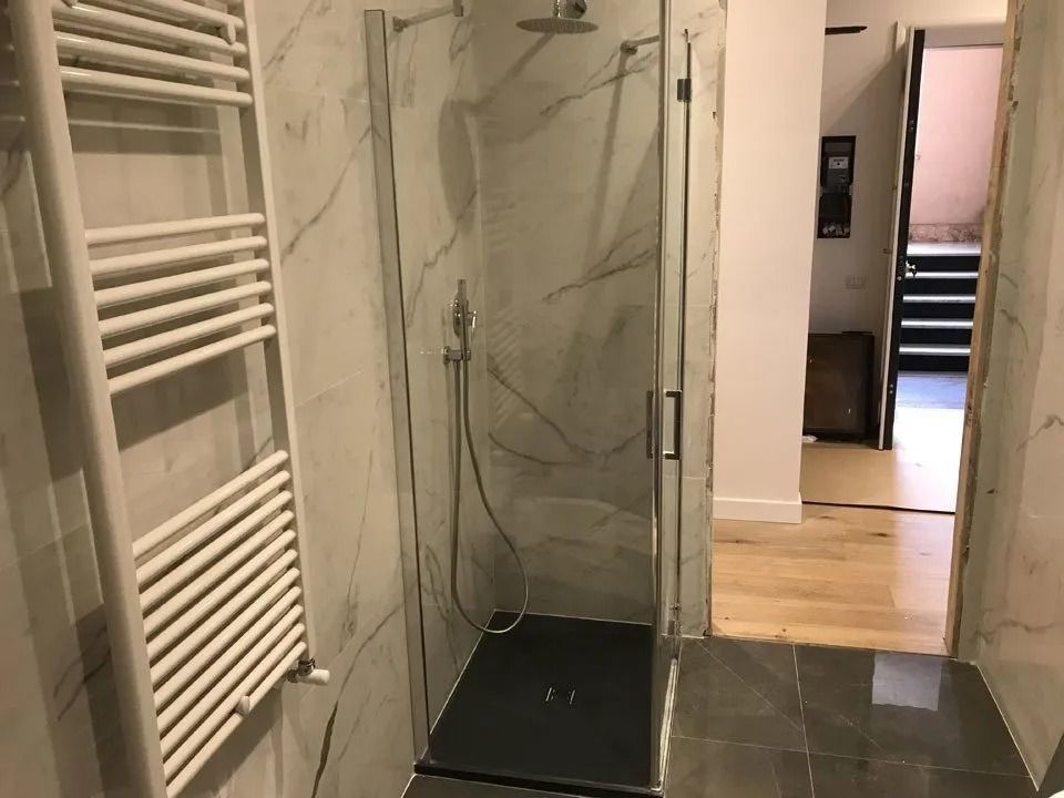 Modern bathroom with tiled shower, white towel radiator, and open doorway to a hallway