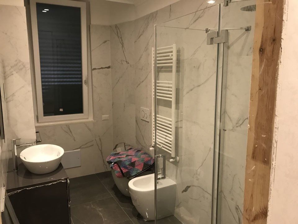 Modern tiled bathroom with a shower, sink, toilet, towel radiator, and window.