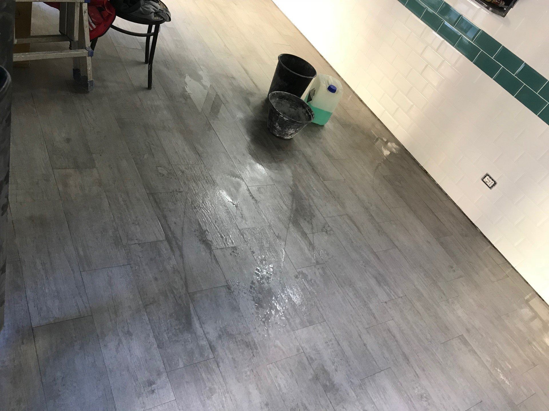 Wet tiled floor in a room with a chair and a bucket near a wall.