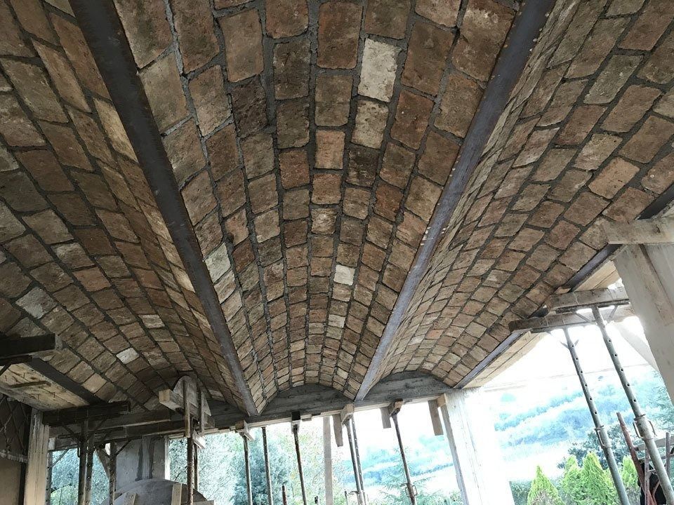 Brick arched ceiling under construction, with metal supports and bright sky visible at the edges.