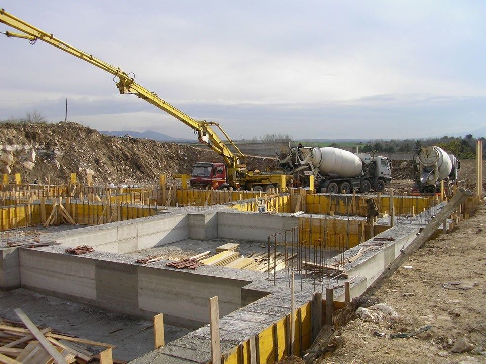 Construction site with concrete foundation forms and a long yellow boom pump truck pouring concrete