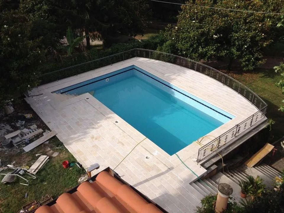 Rectangular outdoor swimming pool with turquoise water beside a white deck and metal railing, surrounded by greenery