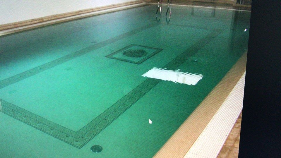 Indoor swimming pool with green water, lane markings, and a white float near the surface