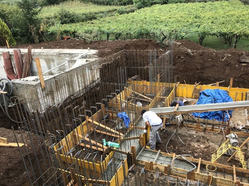 Construction site with workers in a deep excavation, concrete formwork, rebar, and blue tarps.