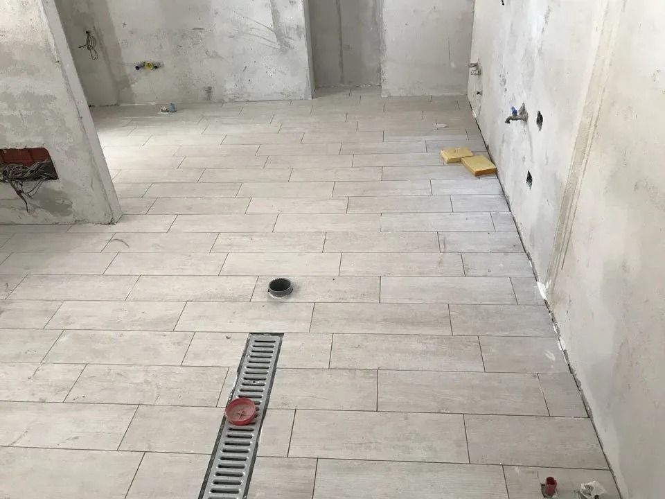Empty tiled bathroom with a floor drain and toilet rough-in pipes.