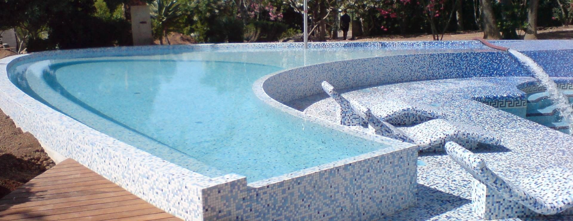 Curved turquoise and blue mosaic swimming pool with a shallow ledge and rippling water