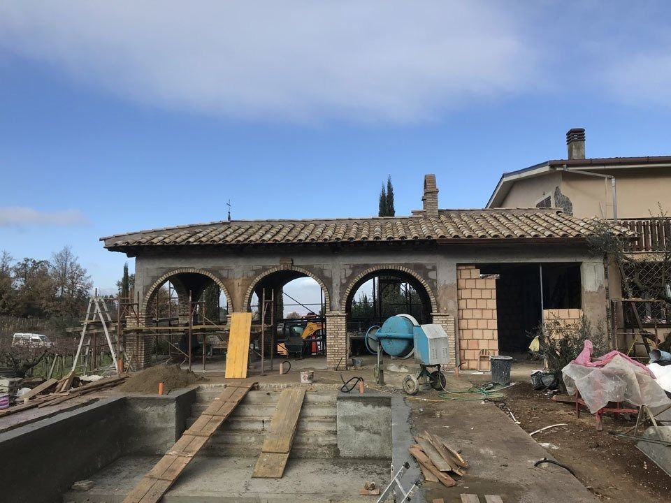 Construction site with arched stone outbuilding, wooden planks, tools, and debris under a blue sky