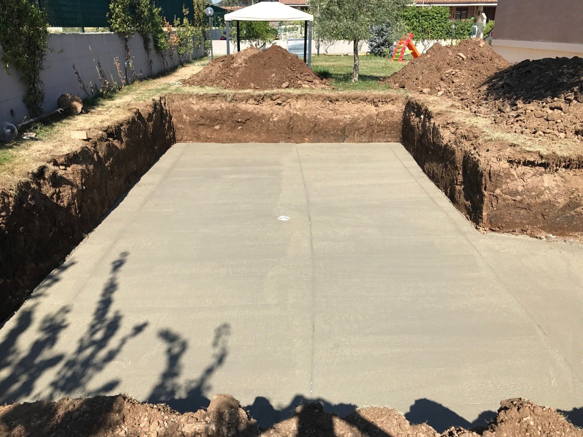 Concrete driveway slab in a trench at a construction site, with dirt mounds on both sides.