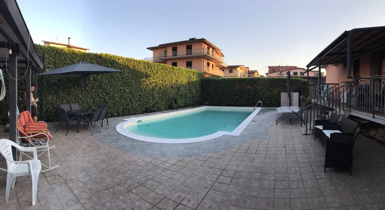 Outdoor pool with turquoise water, stone patio, lounge chairs, and surrounding hedges at dusk