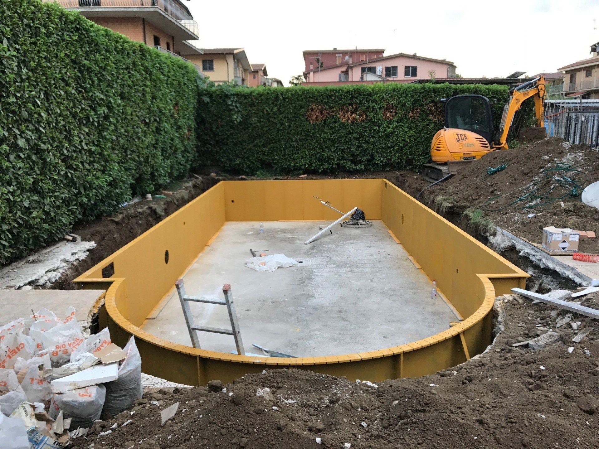 Yellow pool shell under construction in a backyard, with an excavator and dirt around it