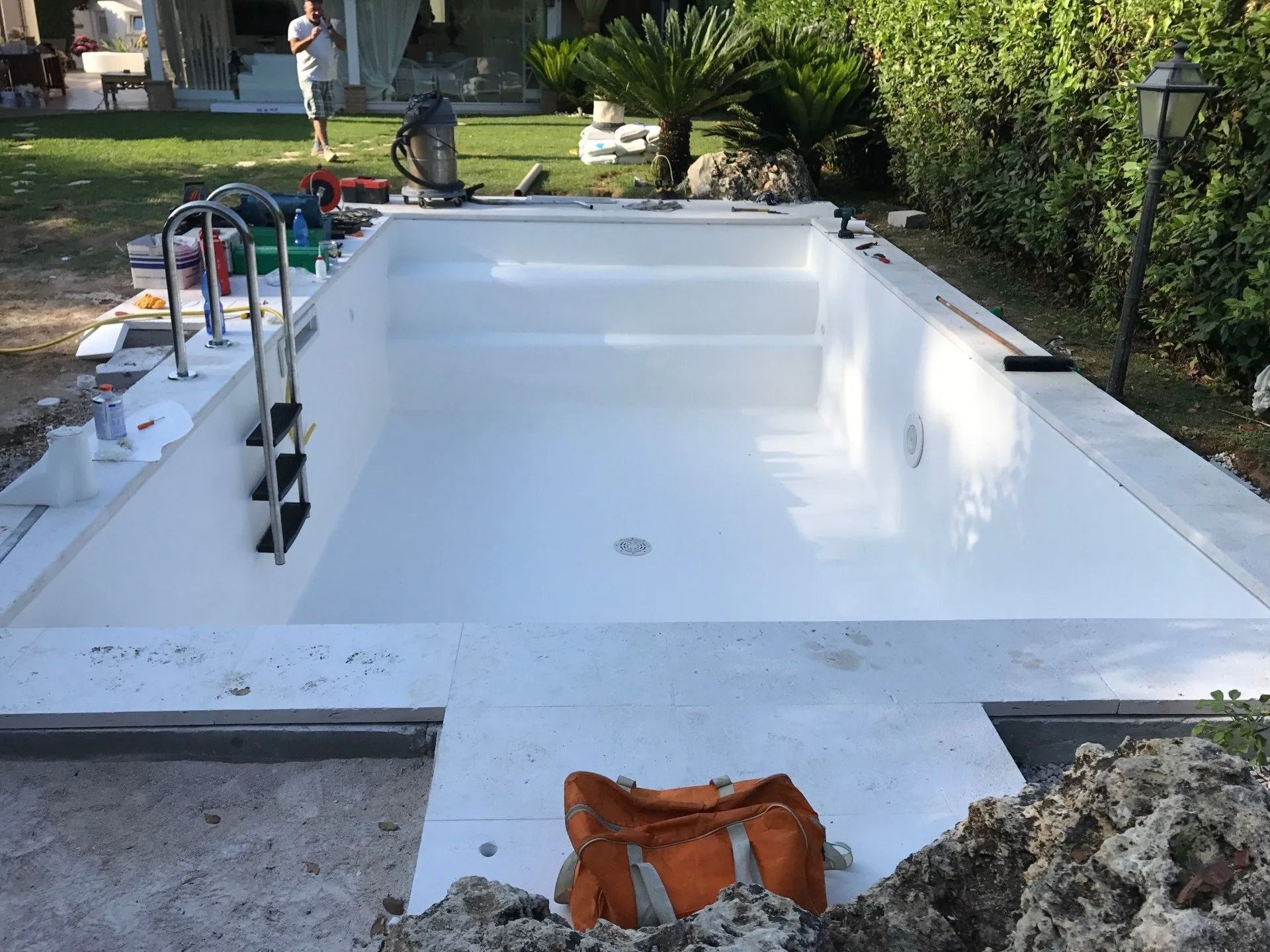 Empty white swimming pool with a ladder, steps, and a life jacket on the deck in a garden setting