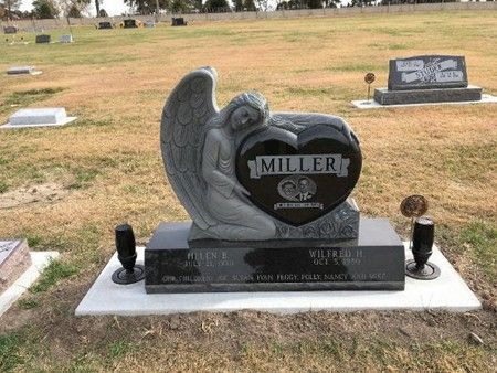 A heart-shaped black granite tombstone with a carved angel, inscribed "MILLER," in a cemetery on a grassy field.
