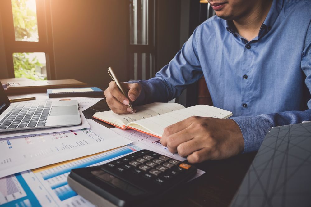 A Person in Blue Shirt Writing in Notebook — Tenth Avenue Accountants & Financial Advisors in Toukley, NSW