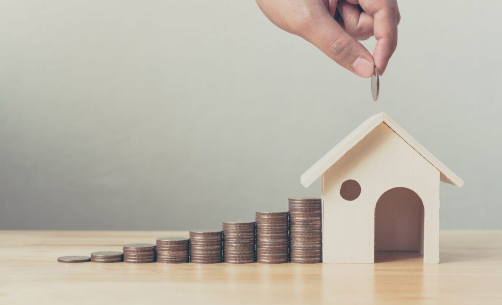 A Hand Placing Coin on Toy House — Tenth Avenue Accountants & Financial Advisors in Toukley, NSW