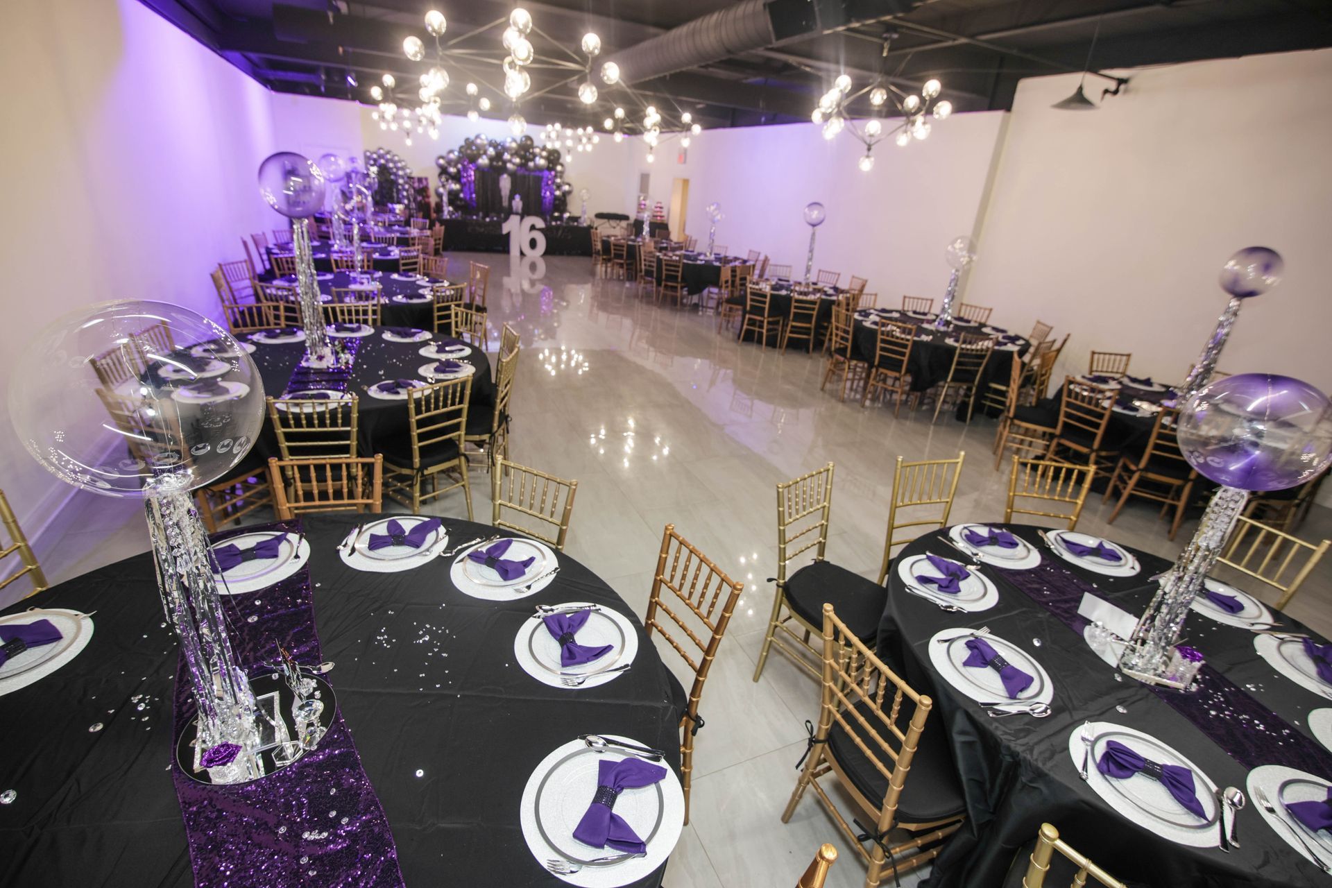Event space set for a party with round tables, black tablecloths, and purple accents.