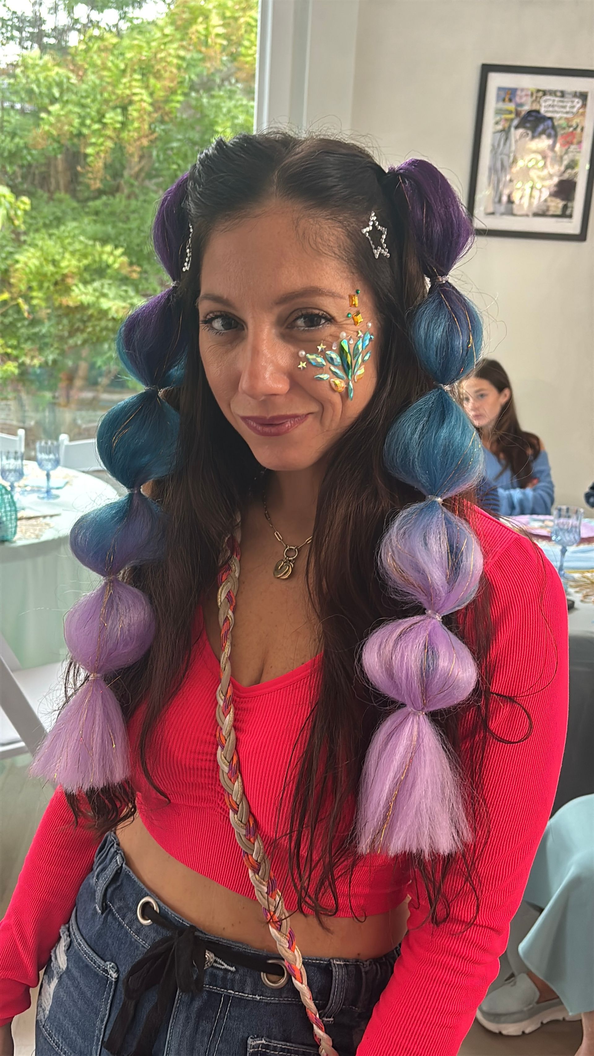 Woman with braided, pom-pom adorned hair and face paint smiles.