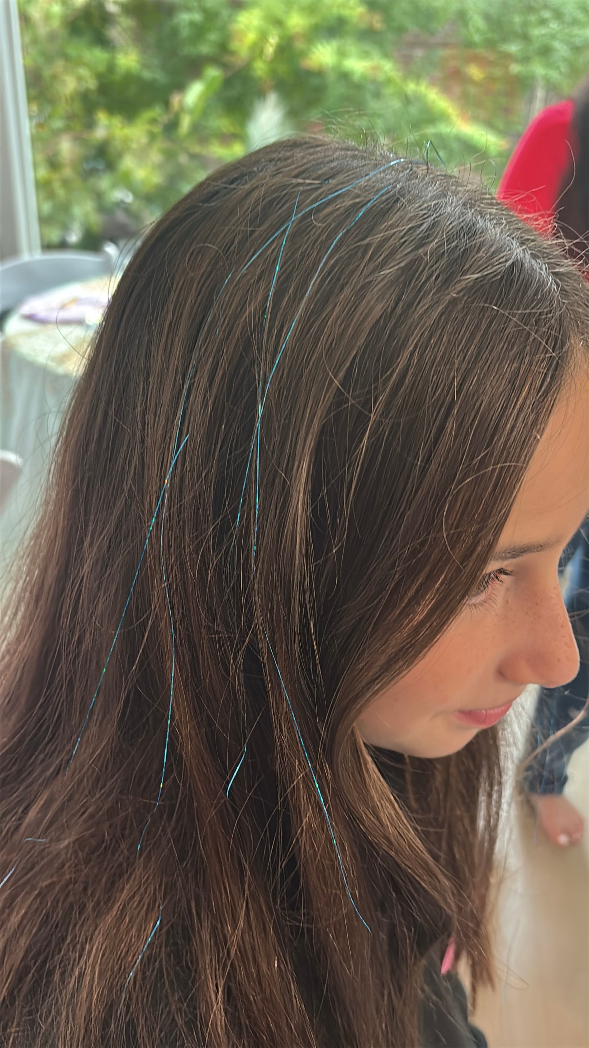 Girl with dark brown hair, some strands with blue tinsel strands.