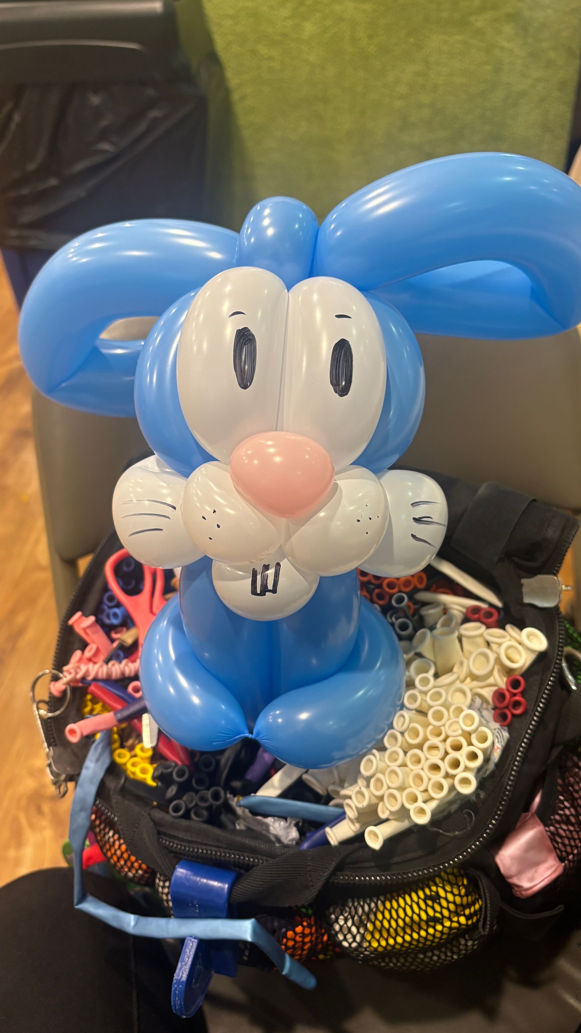 Blue and white balloon animal bunny with pink nose and large ears sitting on a pile of balloons.