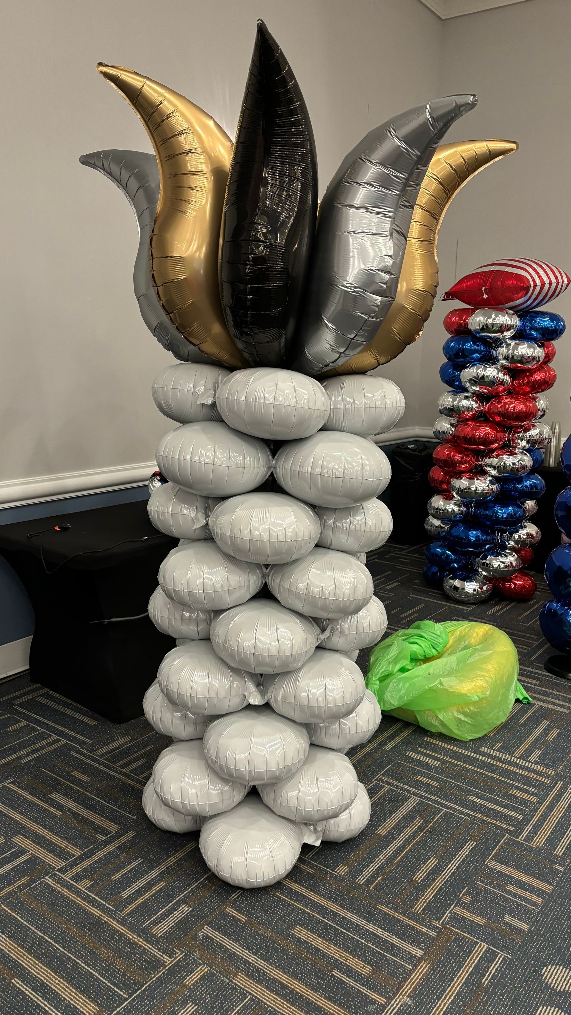 Balloon sculpture: Silver pillar base, topped with gold, black, and silver tulip-shaped balloons.