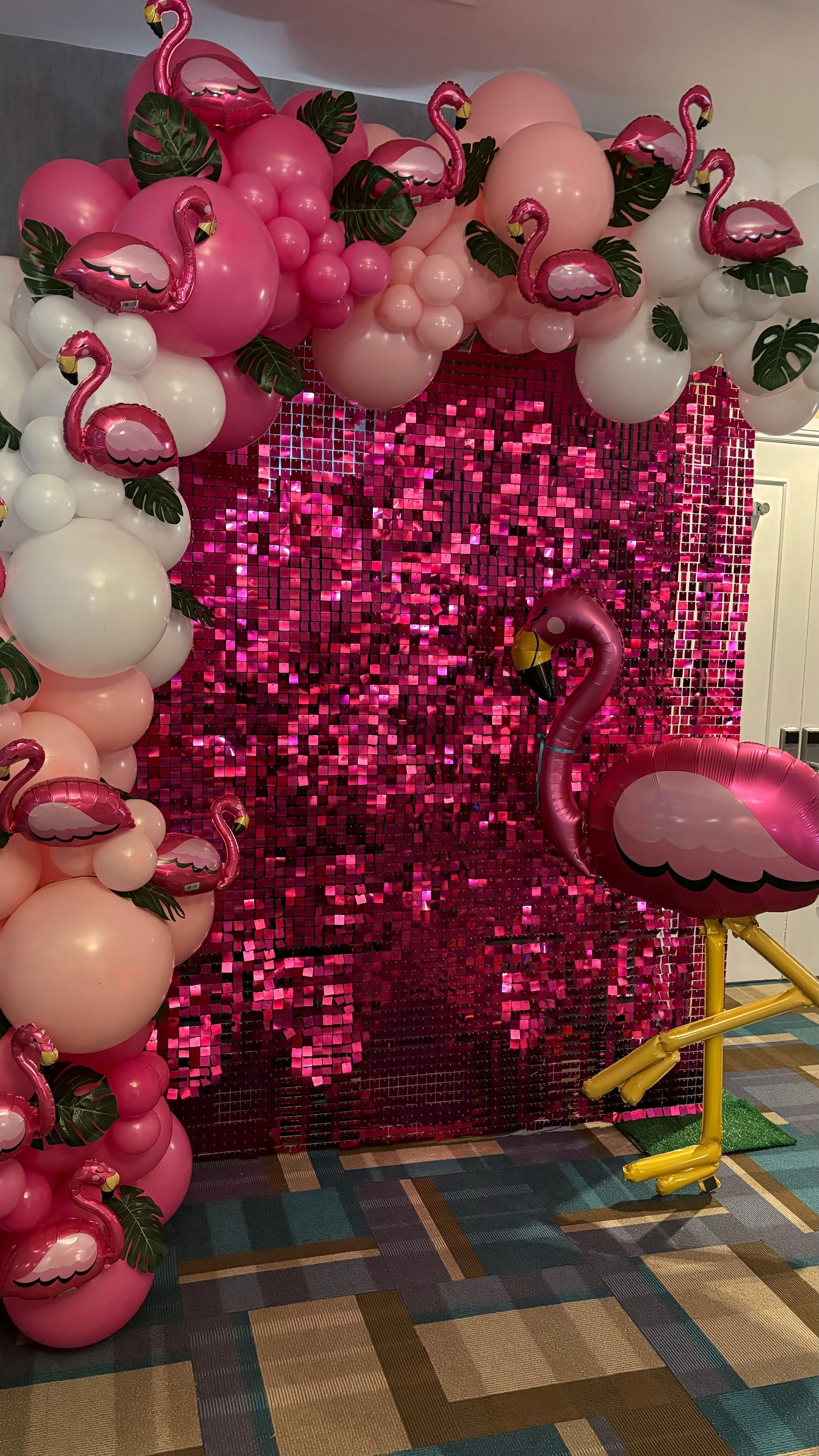 Flamingo-themed party backdrop: pink sequin wall, balloon arch with flamingo and leaf decorations, and a large flamingo balloon.