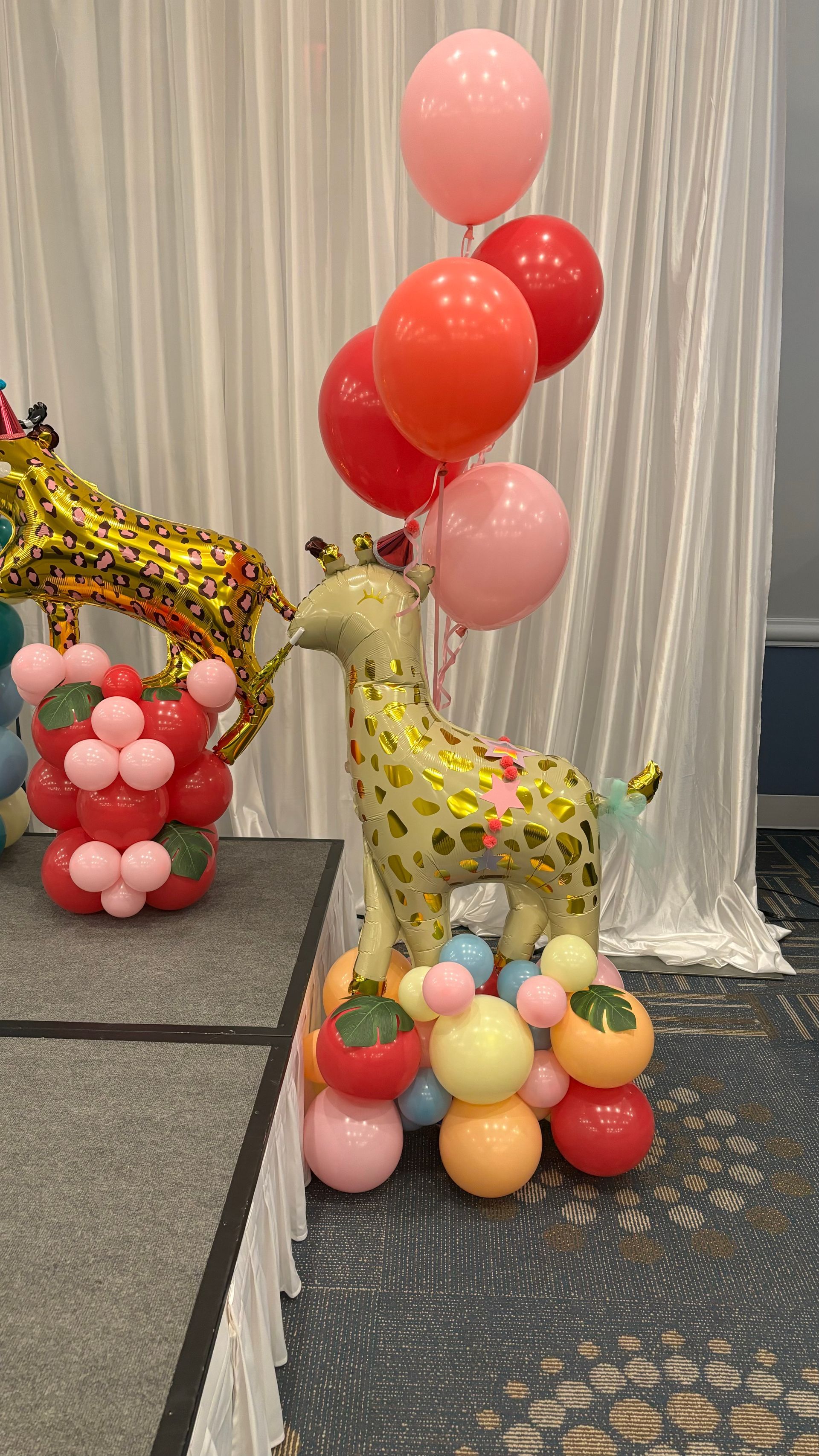A giraffe made out of balloons is sitting on top of a pile of balloons.