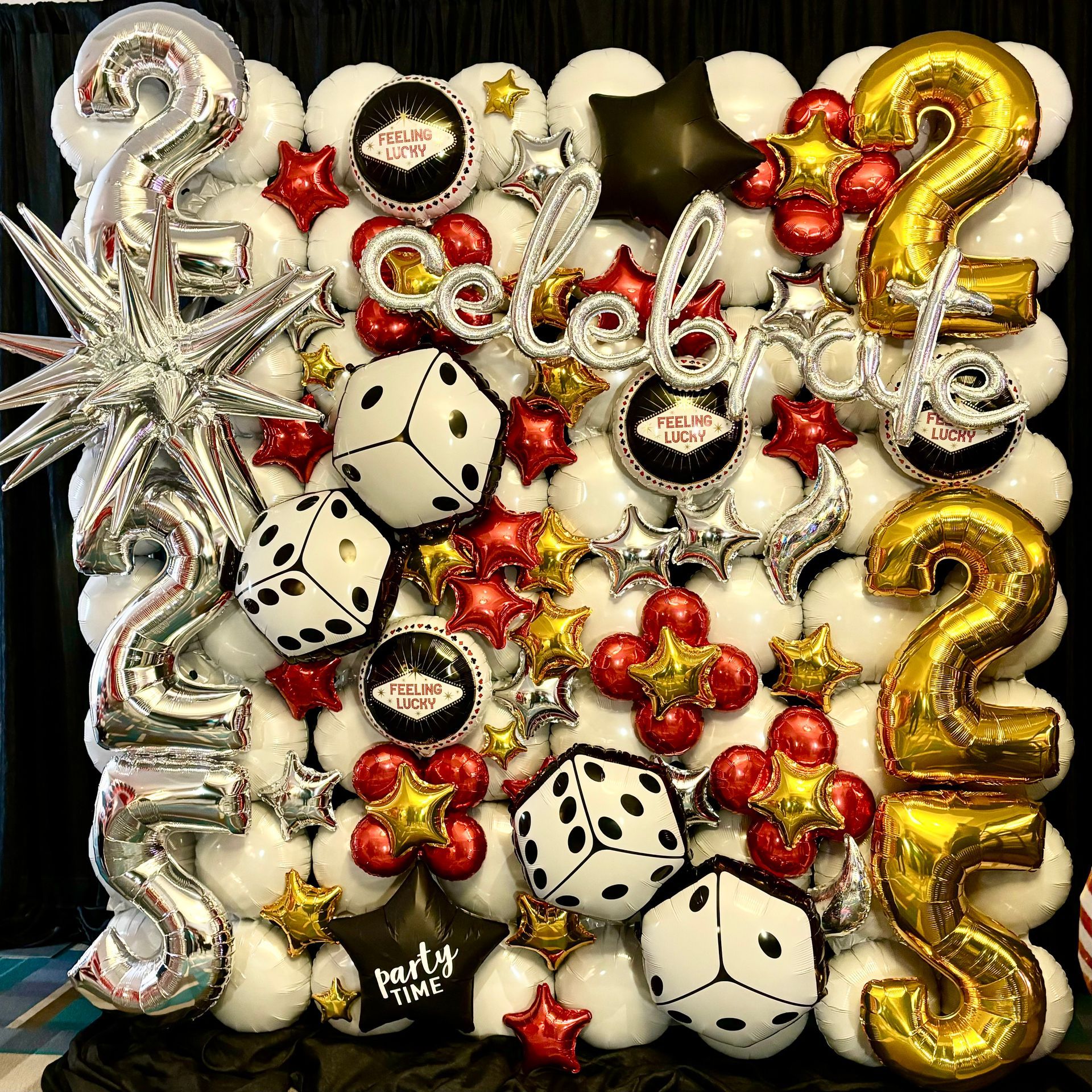 Casino-themed balloon wall with white, red, gold, and black balloons, dice, and starburst accents. The word 
