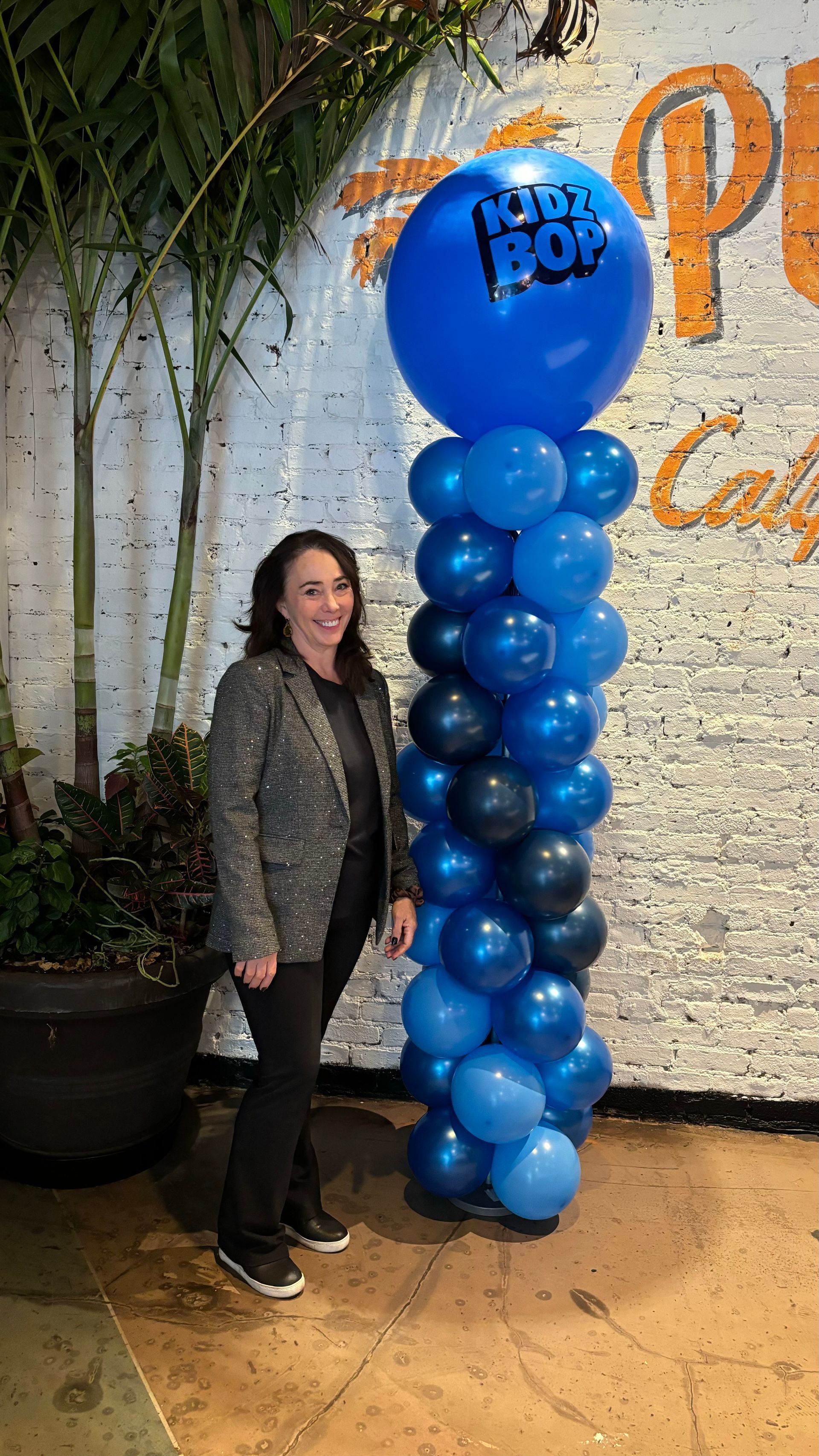 Woman stands near a tall balloon column with a large blue topper; text reads 