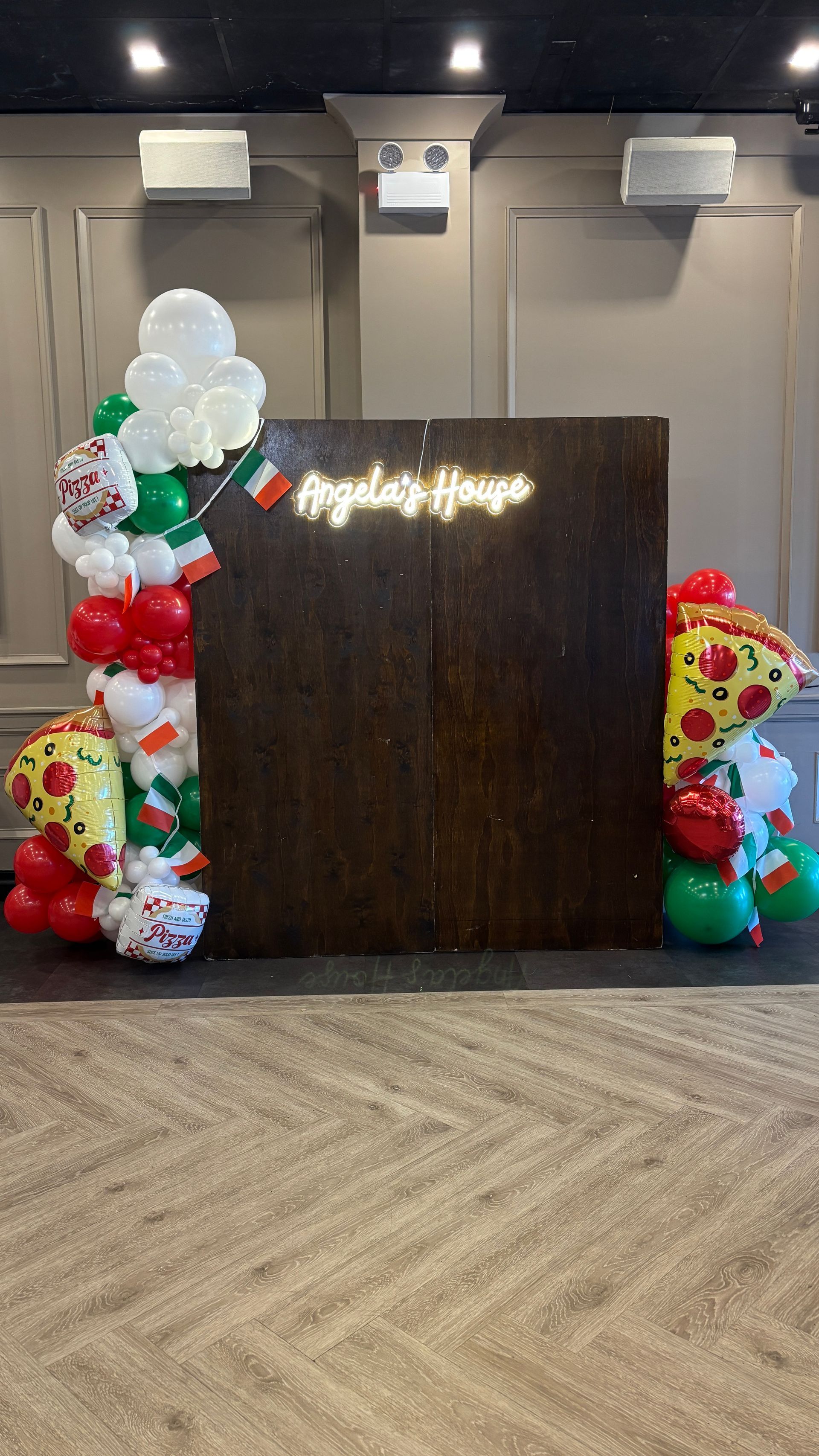Event backdrop with pizza and Italian flag balloons, and a wooden panel.