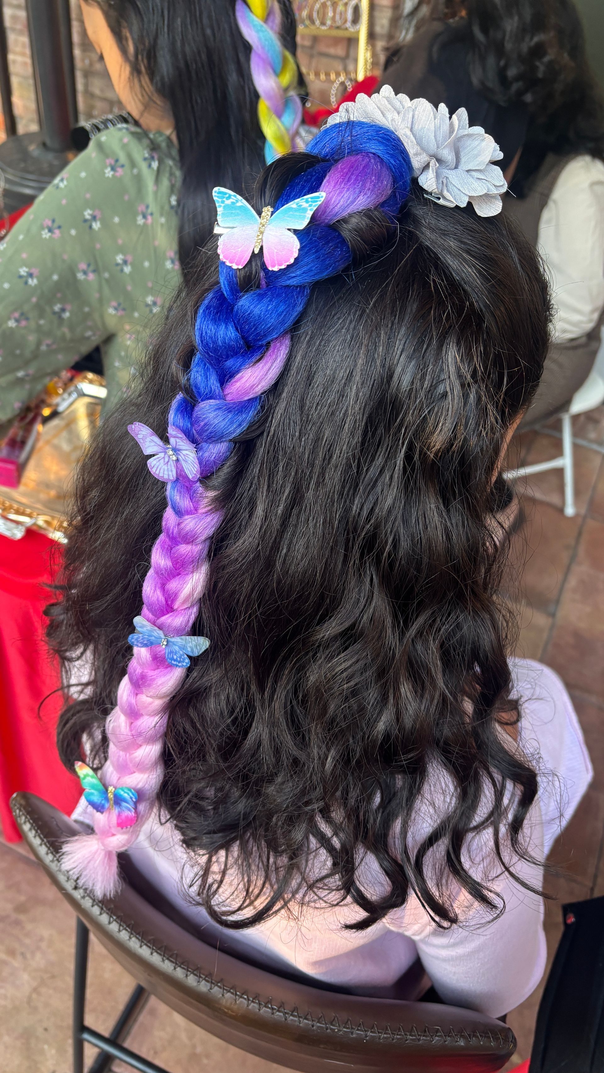Girl with dark hair; a braided colorful extension and butterfly clips.