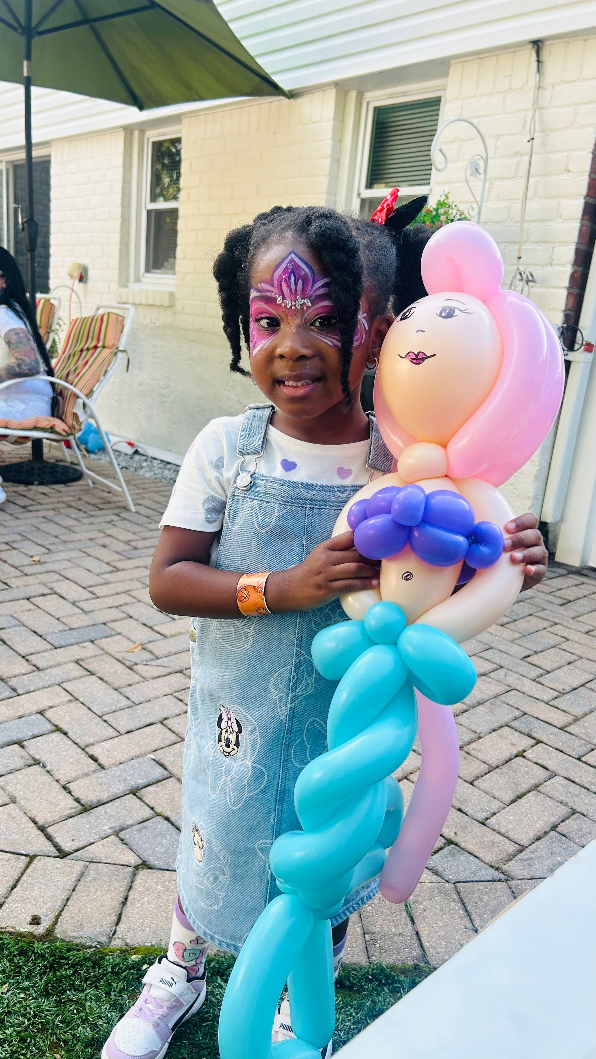 Girl with painted face holding a mermaid balloon sculpture in backyard.