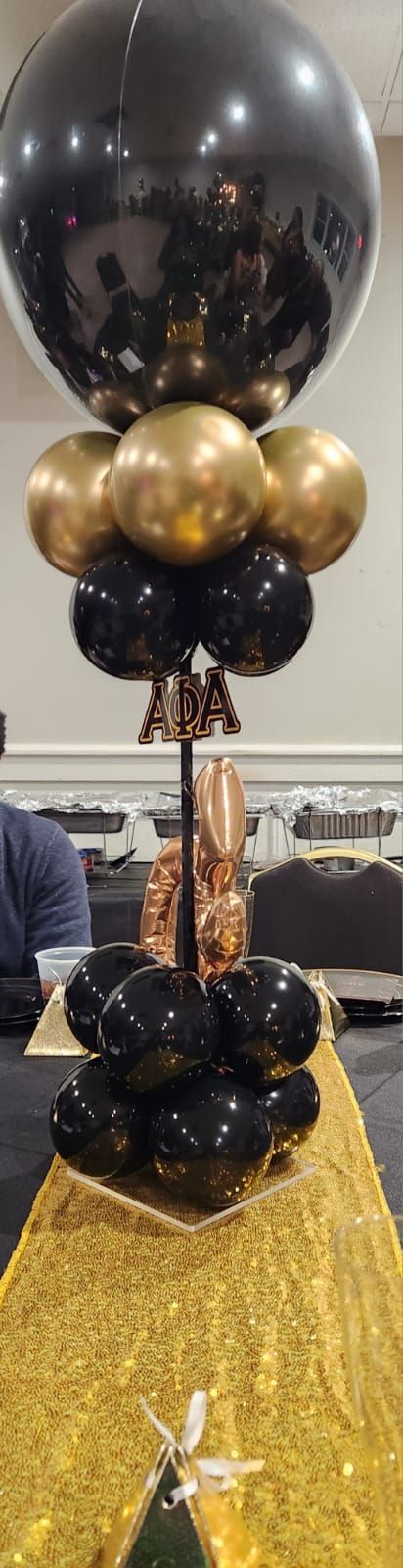 Black and gold balloon centerpiece on a gold tablecloth, possibly for a celebration.