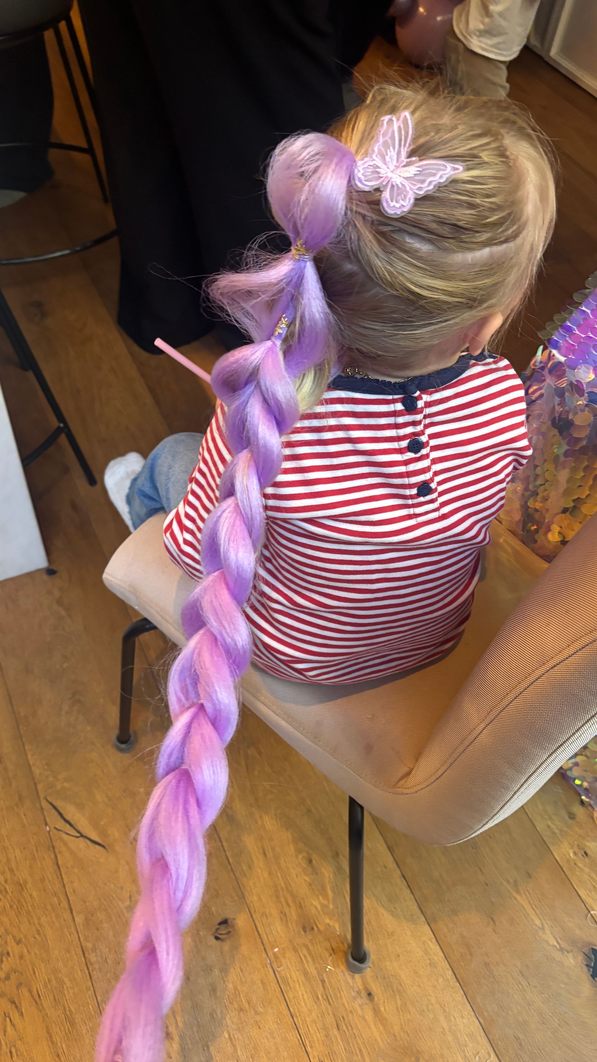 Child with long purple braid and butterfly hair clip. Sitting on a chair.