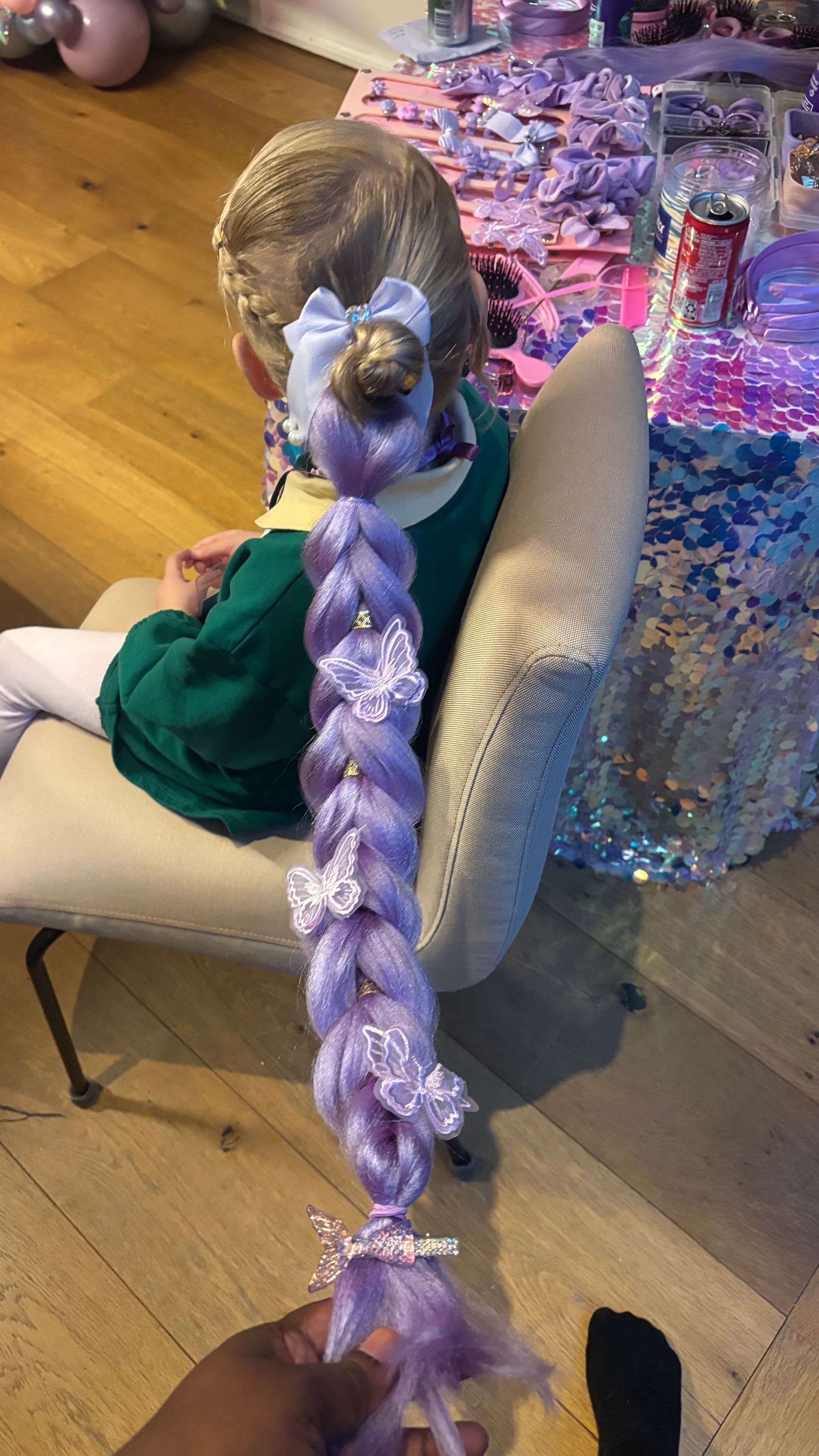 Child with a purple braid, seated at a party. The braid is decorated with bows and embellishments.