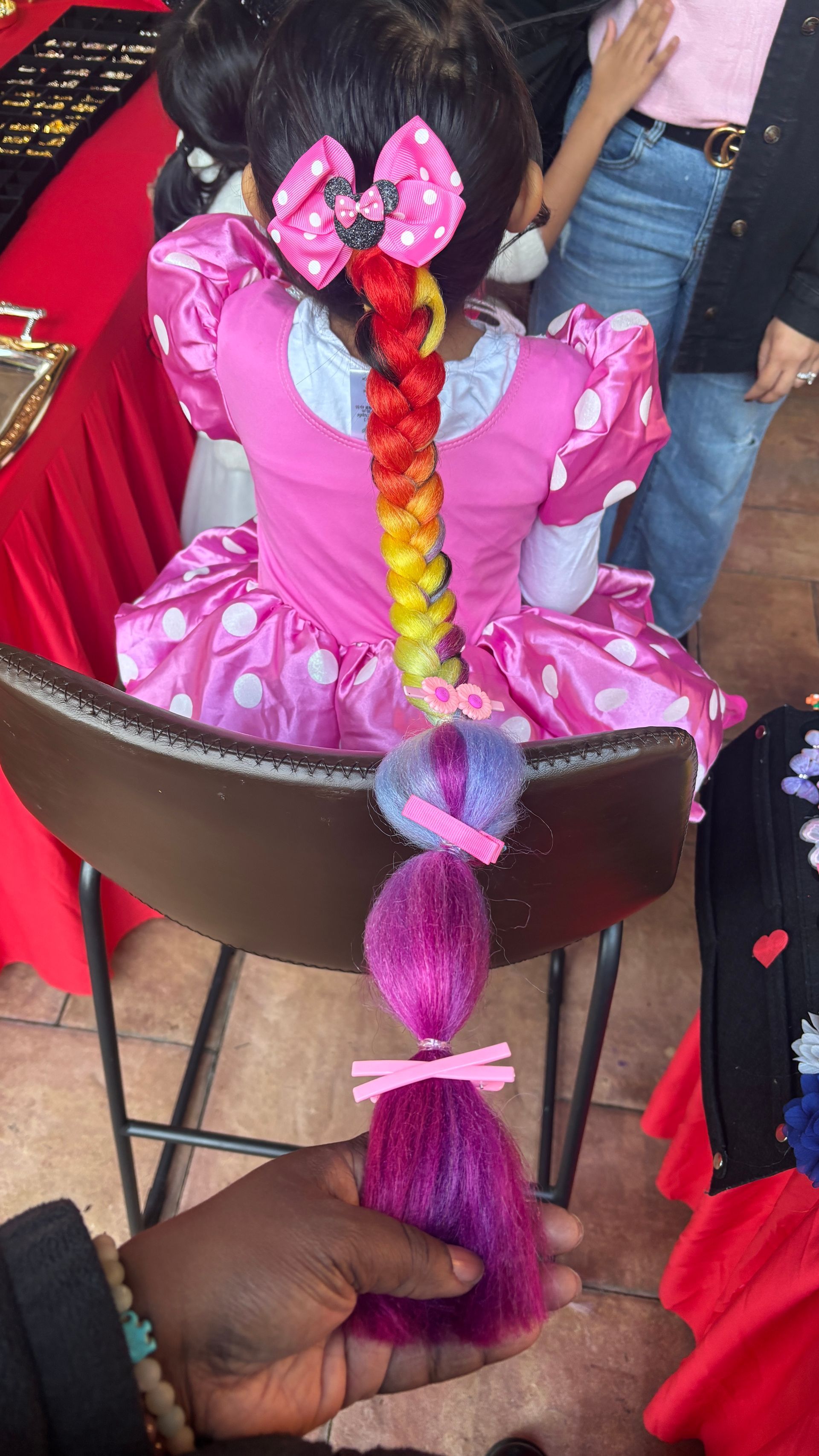 Girl with a rainbow-colored braided hairstyle and pink Minnie Mouse dress.