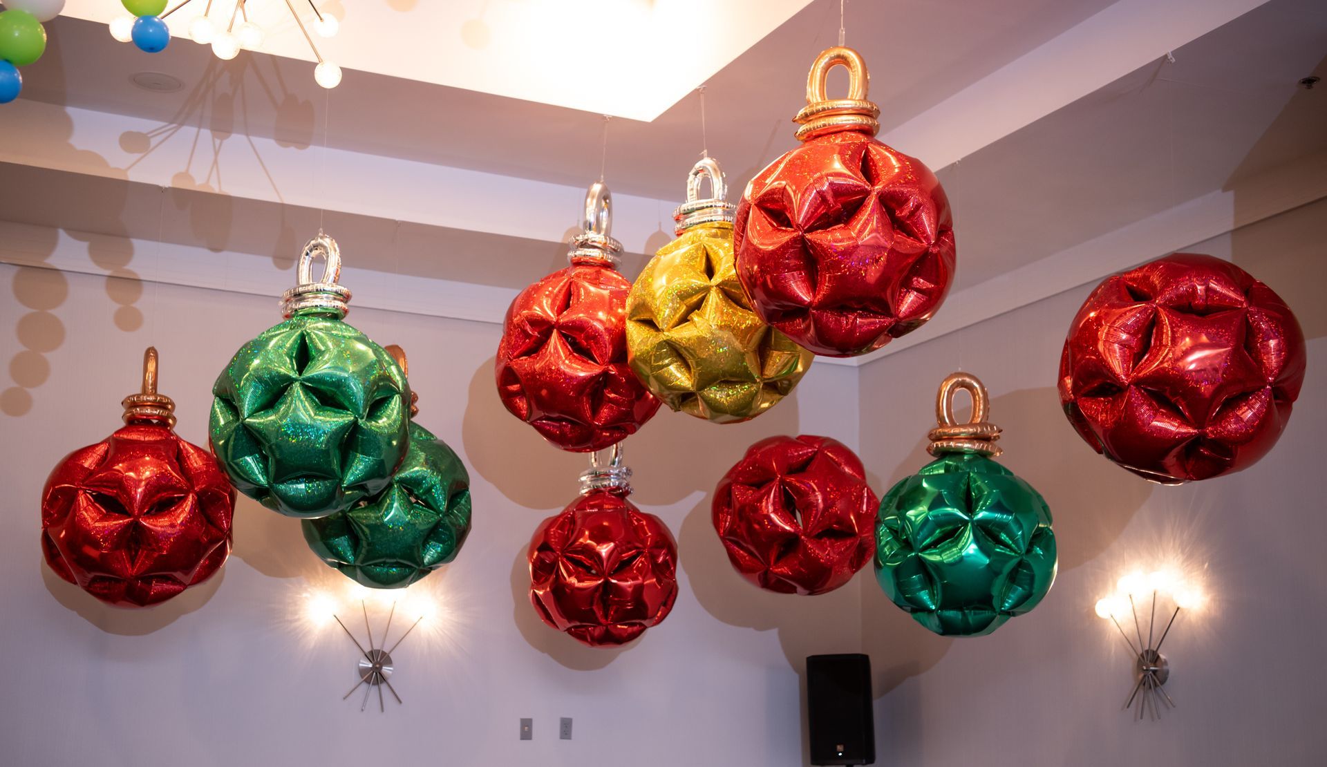 Large, glittery Christmas ornament decorations hanging from a white ceiling, in shades of red, green, and gold.