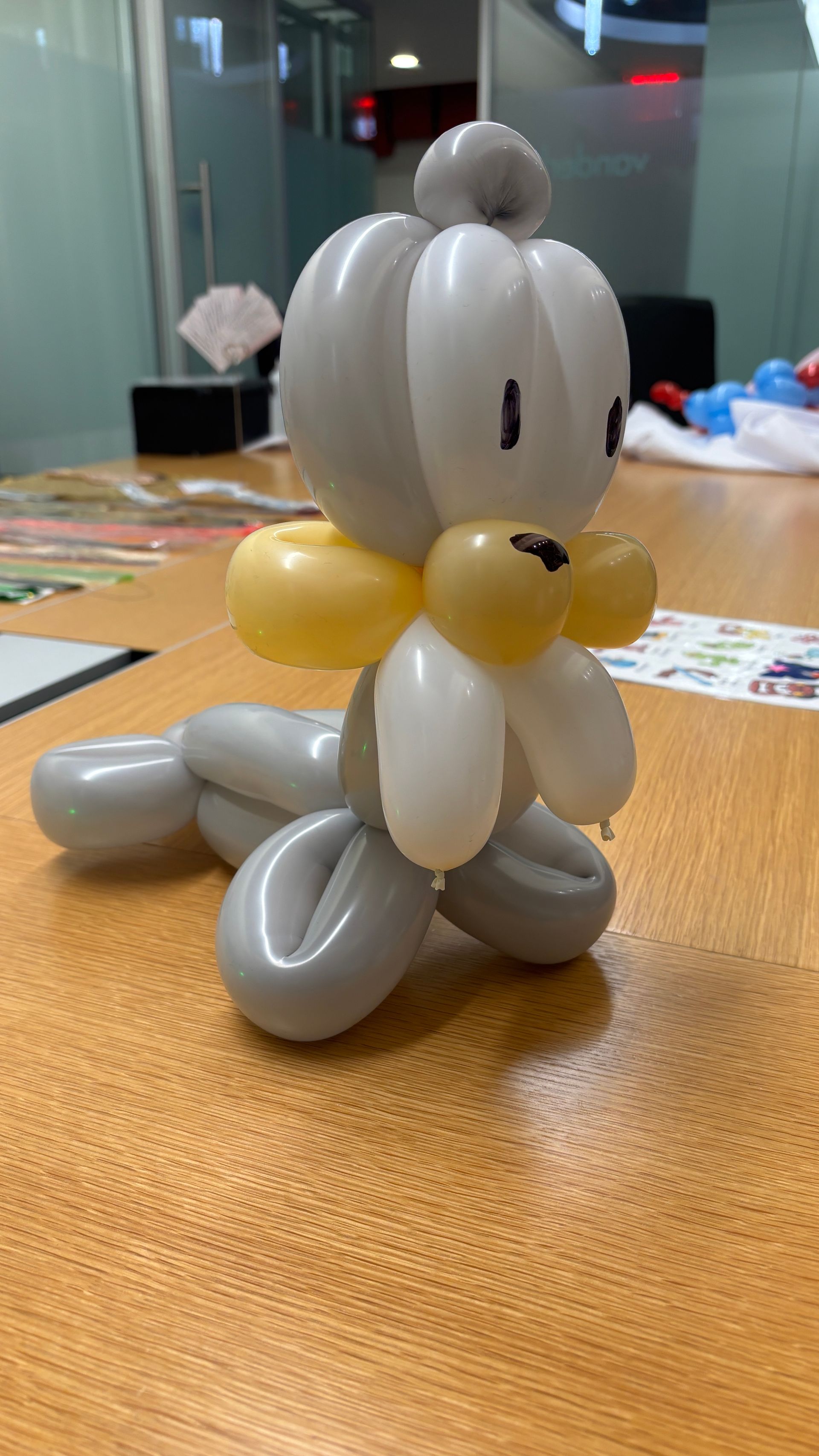 Balloon sculpture of a seal in gray, yellow, and white on a wooden table.